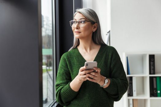 Photo of gray-haired serious businesswoman using cellphone